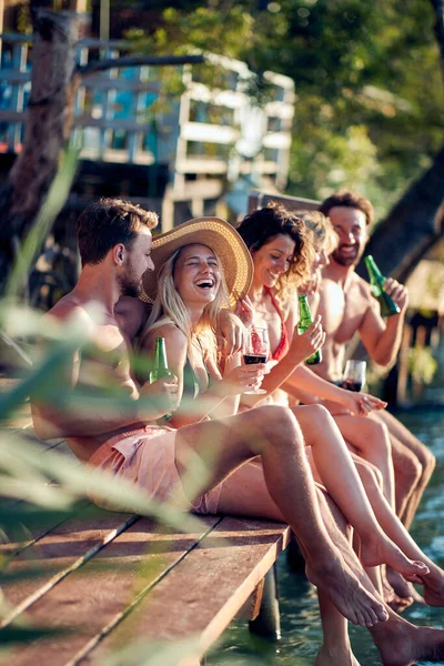 湖の桟橋に座って ビールを飲むことで友人のグループ 一緒に夏休みに若い男と女 楽しみ ライフスタイルのコンセプト — ストック写真