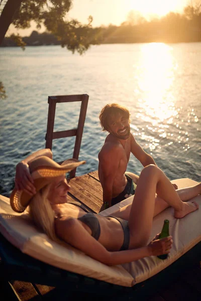 美しい夏の日に川岸で夕日を楽しみながら 水着の若いカップルがチャット — ストック写真