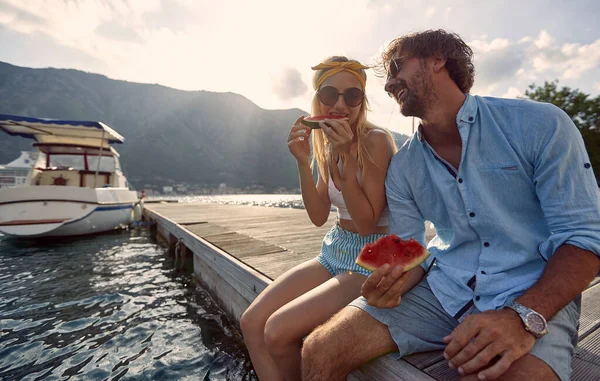 カップル笑ってスイカを食べる 木製の桟橋に水で座っている ライフスタイルの概念 — ストック写真