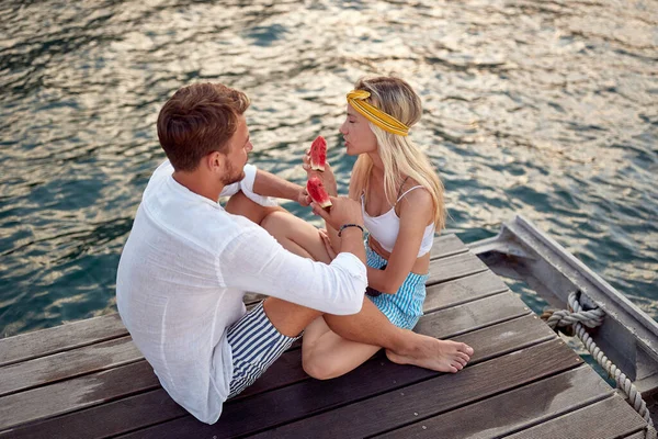 木製のドックで話をし 海でスイカを食べる素敵なカップル 楽しみ ライフスタイルの概念 — ストック写真