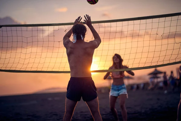 一对年轻夫妇正在海滩上打排球 而夕阳西下是一个美丽的夏日 — 图库照片