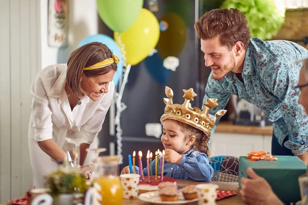 誕生日の女の子は誕生日の女の子として黄金のインフレータブルクラウンを着て テーブルに座って 祖父の周りの両親と 彼女を応援 お祝いの概念 — ストック写真
