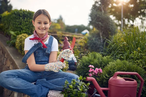 小女孩坐在花园旁边 抱着园艺工具 心情愉快 在阳光灿烂的夏日种花 生活方式 童年概念 — 图库照片