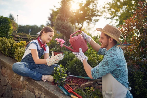 娘と父は一緒に花の庭で屋外で働いて 女の子は花の鍋を保持し 男は水筒でそれを散水 ライフスタイルの概念 — ストック写真