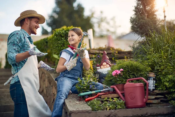 年轻的父亲和女儿在房子旁边的花园一起干活 孩子拿着小花园耙准备种花 生活方式概念 — 图库照片