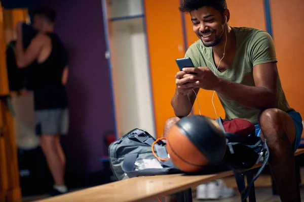 Χαρούμενος Νεαρός Που Κάθεται Στο Καμαρίνι Του Γυμναστηρίου Κοιτάζει Smartphone — Φωτογραφία Αρχείου