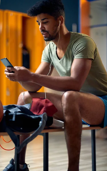 年轻英俊的运动健将 带着耳机和智能手机坐在体育馆更衣室里 准备锻炼 生活方式 健康概念 — 图库照片
