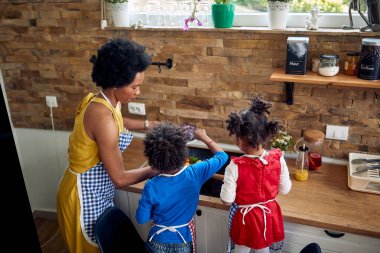 Afro-Amerikan aile mutfağı. Anne, tatlı küçük oğlu ve kızıyla birlikte yemek hazırlıyor..