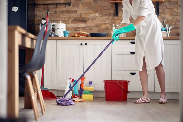 无脸的年轻女子头戴手套 在厨房里打扫卫生 在地板上闷闷不乐 后面是化学瓶子 生活方式概念 — 图库照片