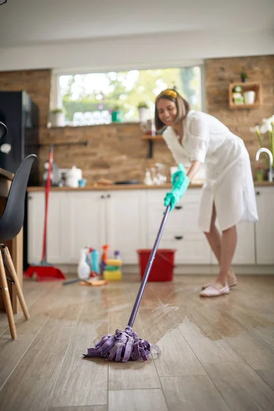 喜びの主婦は台所を掃除し 床を濡らし 背景には化学ボトルが付いています ライフスタイルの概念 — ストック写真