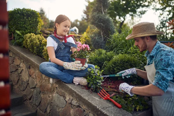 父亲和他的女儿在花园里联合起来 小女孩小心翼翼地捧着一个花盆 而她的父亲则巧妙地在地里打了一个洞 准备播种 — 图库照片
