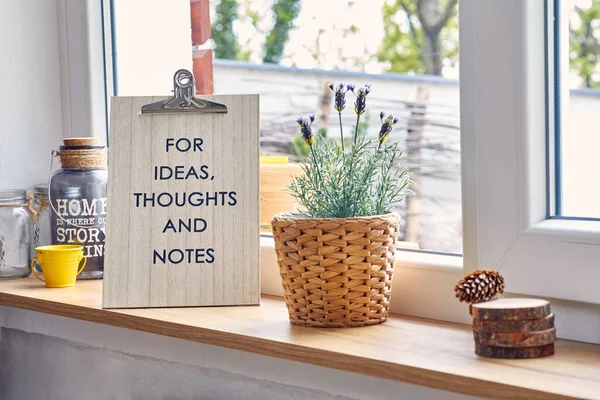 Concept of lavender flowers adorning a window,accompanied by a wooden sign that reads For Ideas,Thoughts, and Notes.These elements come together harmoniously within the setting of a cozy family home.