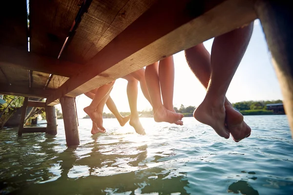 美しい夏の日に川のドックに座っている友人の裸足のグループのクローズアップショット — ストック写真