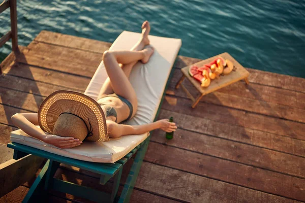 在一个美丽的夏日 一个穿着比基尼的小女孩躺在日光浴床上 享受着阳光 喝着饮料 吃着水果 鸟瞰着她的眼睛 — 图库照片