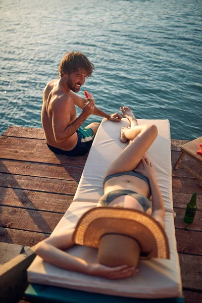 美しい夏の日に川の岸で日光浴を楽しみながら水着を着た若いカップル — ストック写真