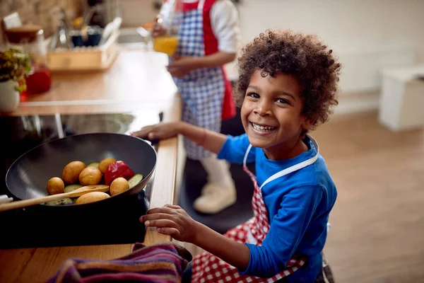 一个面带笑容的非裔美国男孩 他直直地凝视着镜头 流露出一种自信的感觉 在他面前放着一个盛满生机勃勃 五彩缤纷的蔬菜的大煎锅 — 图库照片