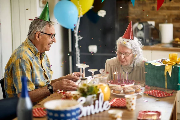Joyful Senior Vrouw Blaast Kaarsen Verjaardagstaart Zit Aan Keukentafel Met — Stockfoto