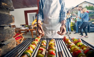 Kimliği belirsiz bir genç adamın et ve sebze şişlerine dönüşmesi, arkadaşlarıyla dışarıda bbq partisi vermesi. Yaşam tarzı, parti, birliktelik konsepti.