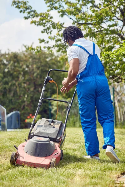アフリカ系アメリカ人は確信を持って芝刈り機を経営している 焦点を当てた表現とハンドルのしっかりしたグリップで 彼は楽に芝生を渡ってマウスをグライド — ストック写真
