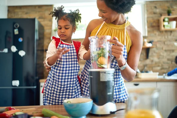 Mother and her young daughter coming together to prepare a healthy meal. Immersed in the process, they are seen adding fresh vegetables to a blender to create a delicious, nutrition-packed beverage.