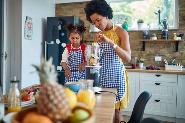 Mother and her young daughter coming together to prepare a healthy meal. Immersed in the process, they are seen adding fresh vegetables to a blender to create a delicious, nutrition-packed beverage.
