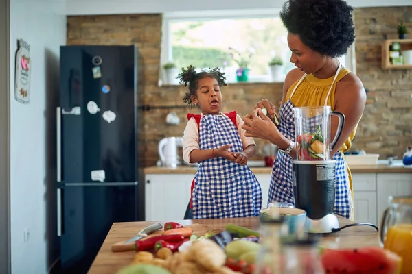 幼い娘と自宅のキッチンにいる若い母親は 野菜を切ってキュウリのスライスを味わい 女の子は馬鹿げている ホーム ライフスタイルのコンセプト ストック画像