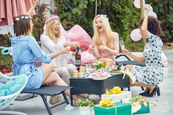 흥분한 4명의 여성들이 옥외에서 파티를 축하하고 샴페인으로 토스트하며 즐겁게 느낍니다 스톡 사진