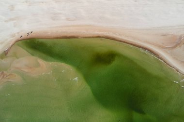 Zümrüt deniz suyu olan büyük kumlu bir sahilin üst manzarası.