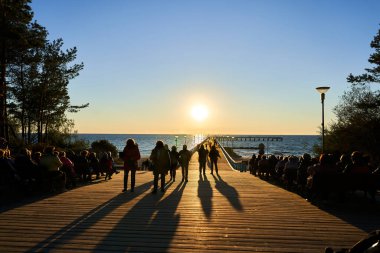 Gün batımında uzun iskele manzarası. Denizin ve rıhtımın arka planında siyah insan siluetleri