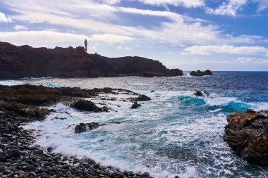 Sahilin silueti ve kayalıklarda alçak bir deniz feneri olan deniz pelerini.