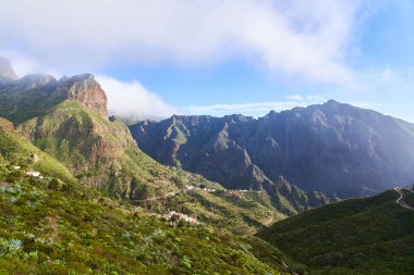 Altında küçük bir köy ve arka planında güçlü kayalar olan dağlardaki manzara.