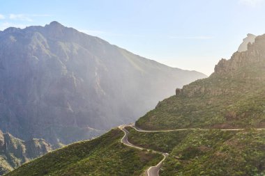 Dolambaçlı bir yolu ve büyük mavi bir dağı olan dağlarda bir manzara. Tenerife 'deki Masque köyüne giden yol.