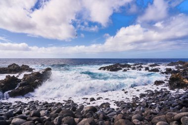 Su, Atlantik Okyanusu 'ndaki boş bir sahilde çakıl taşları ve kayalar üzerinde kırılır.