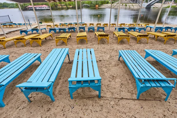 stock image Part of the city beach. Old dirty sunbeds on the background of the city river. A place of rest for citizens