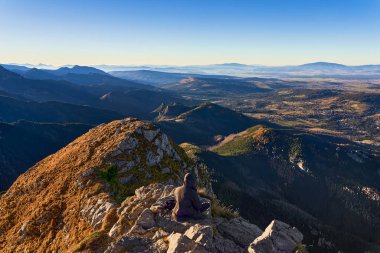 Dağın tepesinde oturan ve doğanın tadını çıkaran bir adam, büyüleyici bir manzara. Doğada rahatlama ve dinlenme
