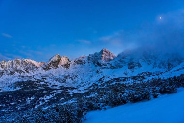 Snowy wonderland in mountain range, moon over mount ridge. Stunning landscape clipart