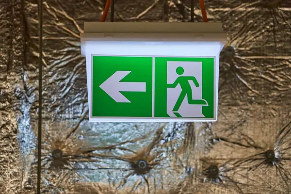 Aydınlatılmış Yeşil ve Beyaz Acil Durum Çıkış İşareti. Sol ve Koşan Adam Piktogramı Duvara monte edilmiş.