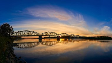 Nehrin üzerindeki köprünün günbatımının arka planına doğru geniş bir panoramik görüntüsü. Köprünün destansı bir fotoğrafı.