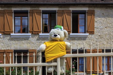 Celles-sur-Ource, Fransa - 26 Temmuz 2022: Sarı forma giyen komik pelüş bir ayı ve özel bir yeşil başlık Le Tour de France Femmes 2022 'nin 4. etabı sırasında bir evin çitlerini süslüyor.