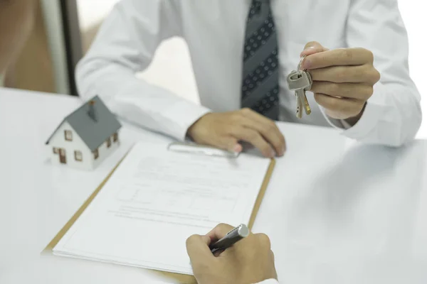 Real estate agent holding house keys to give to client after discussing and signing home loan contract, property insurance to buy home. Real estate concept.