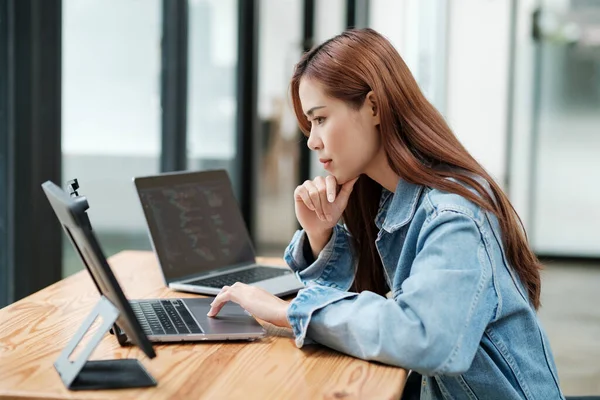 Young female professional programmer, web or app developer, designer working or writing code at office using laptops and tablet while standing at desk.
