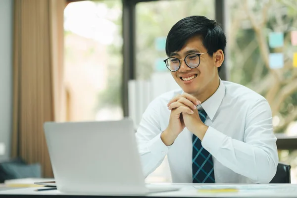 年轻的专业人士 专心致志的商人 戴着眼镜 一边坐在办公室的办公桌前一边 一边用笔记本电脑开心地微笑着工作 一边分析数据 制定商业策略来提高销售利润 — 图库照片