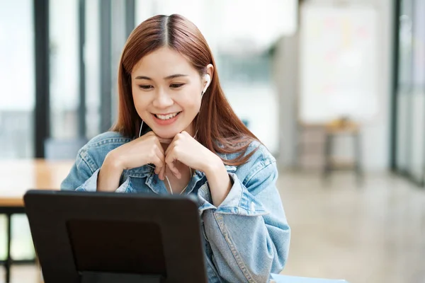 年轻的亚洲女人在网上学习 喜欢用平板电脑 戴着耳机 坐在办公桌前 在室内带着课本和眼镜 在线学习概念 — 图库照片
