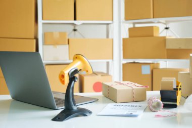 Bilgisayarın, karton kutuların, tarayıcının, halatın, kağıtların ve müşterilerin sipariş paketlerinin depo veya işyerindeki rafların da dahil olduğu çevrimiçi iş quipments fotoğrafları. Çevrimiçi satış, e-ticaret konsepti.