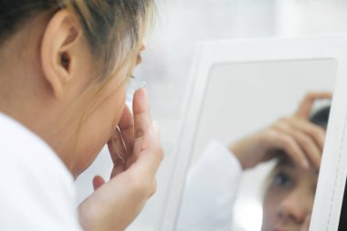 Genç ve güzel bir kadın göz doktorunun baskısıyla alınan lensleri göz hekimliği kliniğindeki aynaya bakmaya çalışıyor..