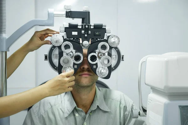 Smart handsome man having eye test, visual examination, check by a professional optician using clinical testing machine phoropter for making new eyeglasses at optic store.