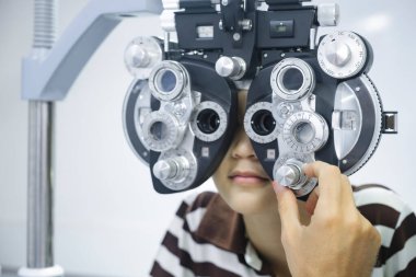 Göz testi yaptıran yakışıklı bir çocuk, görsel muayene, klinik test makinesi phoropter kullanan profesyonel bir gözlükçü tarafından optik mağazada yeni gözlük yapmak için kontrol ediliyor..