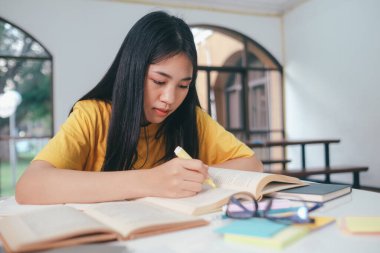 Asyalı kız öğrenci sınava hazırlanmak için oturup kitap okuyordu. Bir sürü kitap okumaktan bıkmıştı..