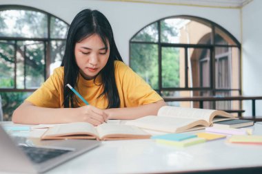 Genç Asyalı üniversite öğrencisi sınavlar için bir kitap okuyor. Üniversite öğrencilerinin kendi kendilerine öğrenmeleri ve öğrenmeleri üniversitenin çalışma odasında gerçekleşir..
