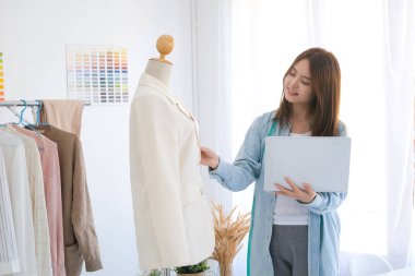 Fashion designer tailor is working in the design studio using laptop to checking customer order on online shop. Business owner, start up small business owner and online business concept.